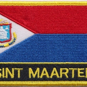 Op de afbeelding: Een geborduurde patch met de vlag van Sint Maarten. De vlag is een blauwe, witte en rode driekleur met een wapenschild in de bovenste hijshoek. De patch heeft een zwarte rand met de woorden "SINT MAARTEN" in gele letters.