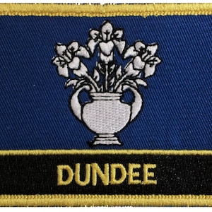 Op de afbeelding: Een geborduurde patch in blauw en goud met een witte vaas met bloemen en het woord "DUNDEE" in gouden letters.