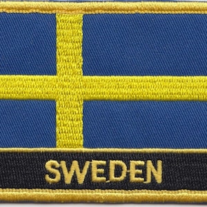 Pode incluir: Um remendo bordado com a bandeira da Suécia em azul e amarelo, com a palavra "SUÉCIA" em letras amarelas sobre um fundo preto.