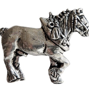 May include: A silver pewter figurine of a horse wearing a harness. The horse is standing on all four legs and has a detailed mane and tail.