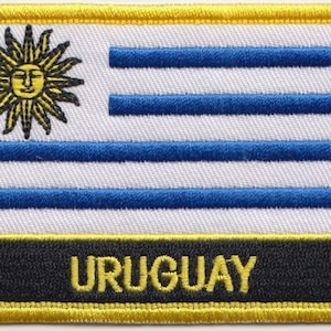 Könnte beinhalten: Ein gestickter Aufnäher mit der Flagge Uruguays. Die Flagge ist weiß mit neun blauen horizontalen Streifen und einer goldenen Sonne mit einem menschlichen Gesicht in der oberen linken Ecke. Das Wort "URUGUAY" ist in gelben Buchstaben auf schwarzem Hintergrund am unteren Rand des Aufnähers geschrieben.
