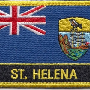 Op de afbeelding: Een geborduurde patch met de vlag van Sint-Helena, met een blauwe achtergrond, een Union Jack in de linkerbovenhoek en een wapenschild rechts. De tekst "ST. HELENA" is in geel geborduurd.