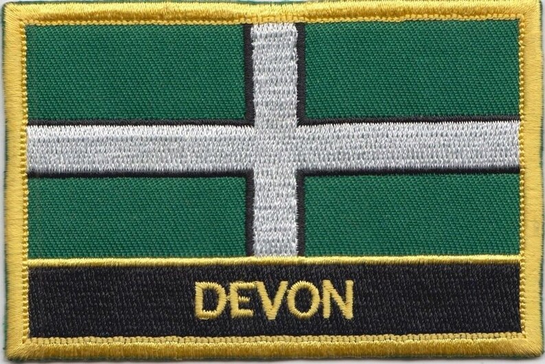 May include: A green and white flag with a white cross and the word "DEVON" in gold lettering on a black background. The flag is surrounded by a gold border.