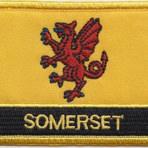 Könnte beinhalten: Ein gelber gestickter Aufnäher mit einem roten Drachen und dem Wort "SOMERSET" in Schwarz.
