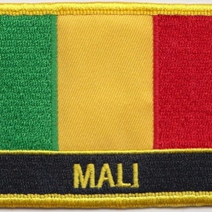 Może przedstawiać: Naszywka haftowana w kolorach flagi Mali: zielonym, żółtym i czerwonym. Naszywka ma czarne tło z napisem "MALI" w żółtych literach i żółtą ramkę.