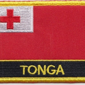 Könnte beinhalten: Ein gestickter Aufnäher mit der Flagge von Tonga. Der Aufnäher ist rot mit einem weißen Kreuz und hat einen schwarzen Rand mit der Aufschrift "TONGA" in gelben Buchstaben.