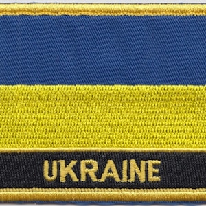 Könnte beinhalten: Ein gestickter Aufnäher mit der ukrainischen Flagge, mit dem Wort "UKRAINE" in gelben Buchstaben auf schwarzem Hintergrund.