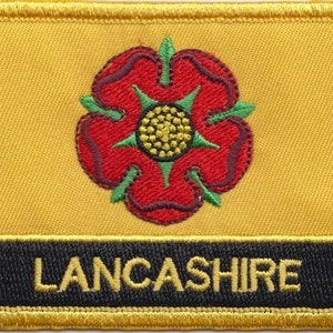 May include: A yellow embroidered patch with a red rose and green leaves. The text "LANCASHIRE" is embroidered in gold on a black background.