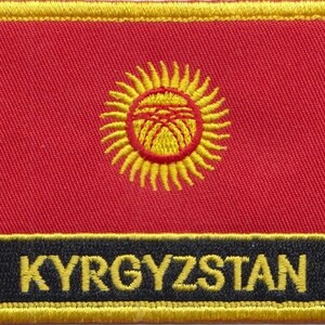 Könnte beinhalten: Ein roter gestickter Aufnäher mit einer gelben Sonne und dem Wort "KYRGYZSTAN" in gelben Buchstaben auf schwarzem Hintergrund.