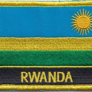 Peut inclure: Un écusson brodé représentant le drapeau du Rwanda, avec l'inscription "RWANDA" en lettres jaunes sur fond noir.