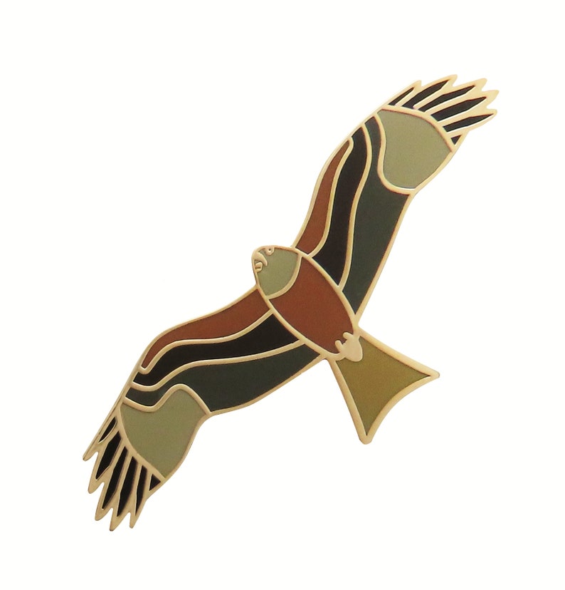 May include: A gold-toned metal pin shaped like a stylized hawk in flight. The hawk has brown, black, and green enamel details.