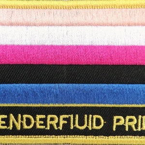 May include: A genderfluid pride flag patch with a gold border. The flag has six horizontal stripes: pink, white, pink, black, blue, and gold. The text "GENDERFLUID PRIDE" is embroidered in gold on the bottom stripe.