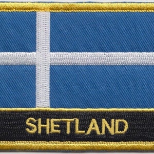 May include: A blue and white embroidered patch with a gold border and the word "SHETLAND" in gold lettering on a black background.