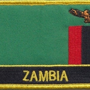 Pode incluir: Um remendo bordado com a bandeira da Zâmbia, com fundo verde, listras vermelhas, pretas e laranja, e uma águia dourada. O remendo tem uma borda amarela e a palavra "ZAMBIA" em letras amarelas sobre um fundo preto.