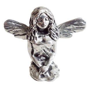 Könnte beinhalten: Eine silberne Feenfigur mit Flügeln, die mit ihren Händen in ihrem Schoß sitzt.