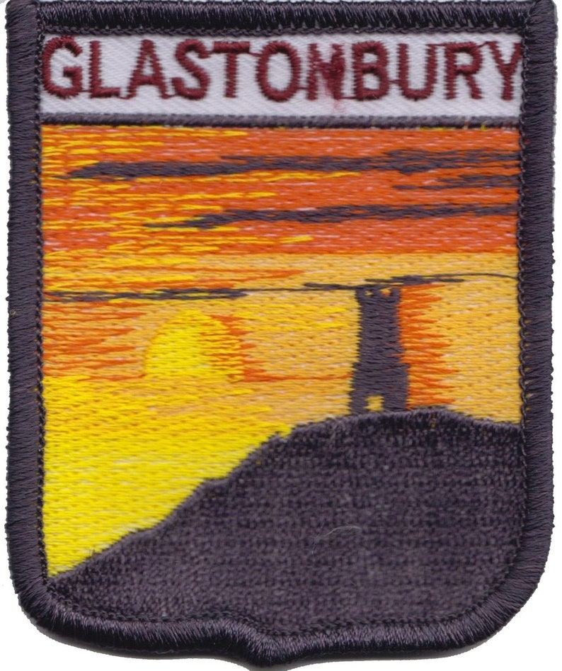 May include: Embroidered patch with a sunset scene and a silhouette of a tower on a hill. The patch is navy blue with a white border and the text "GLASTONBURY" in red.