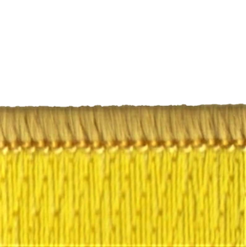 Puede incluir: Primer plano de una cinta de tejido amarillo con un borde de flecos. La cinta tiene una textura sutil y un hilo dorado que la atraviesa.
