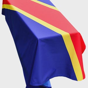 May include: A blue, red, and yellow flag-themed tablecloth. The tablecloth has a blue base with a red stripe down the centre and yellow stripes on either side. The top left corner has a small emblem.