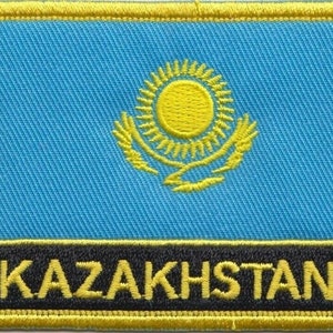 May include: Embroidered patch featuring the flag of Kazakhstan. The design includes a light blue background, a yellow sun with rays, and a golden eagle. The word "KAZAKHSTAN" is embroidered in yellow on a black banner.