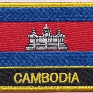 May include: Embroidered patch featuring the Cambodian flag. The flag is red with a blue stripe at the top and bottom. A white temple is in the centre of the red stripe. The words "CAMBODIA" are embroidered in yellow on a black background at the bottom of the patch.