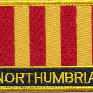 Pode incluir: Um remendo de tecido listrado amarelo e vermelho com a palavra "NORTHUMBRIA" em letras amarelas sobre fundo preto.