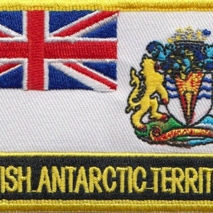 May include: A yellow embroidered patch featuring the Union Jack in the top left corner and the coat of arms of the British Antarctic Territory in the top right corner. The patch has a black background with the text "BRITISH ANTARCTIC TERRITORY" in yellow letters.