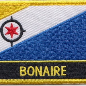 May include: A yellow, white, and blue embroidered patch with a red star in a black circle. The patch has a black border and a yellow border around the black border. The word "BONAIRE" is embroidered in yellow on a black background at the bottom of the patch.