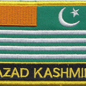 May include: An embroidered patch in green and white with a crescent moon and star in the top right corner. The patch has a yellow border and the text "AZAD KASHMIR" in yellow letters on a black background.