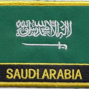 Pode incluir: Patch bordado com a bandeira da Arábia Saudita. O design inclui um fundo verde com escrita árabe branca e uma espada branca. A parte inferior do patch tem a palavra "SAUDIARABIA" em letras amarelas sobre um fundo preto, emoldurado por uma borda amarela.