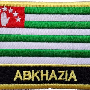 Op de afbeelding: Een geborduurde patch in geel, groen en wit met het woord "ABKHAZIA" in gele letters op een zwarte achtergrond.