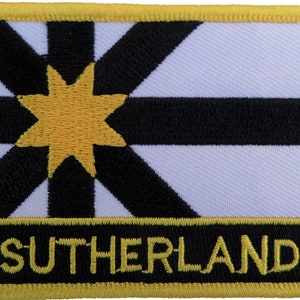 May include: A white and black embroidered patch with a yellow star in the centre. The patch has a yellow border and the word "SUTHERLAND" is embroidered in yellow at the bottom.