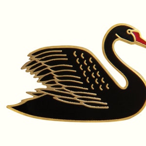 May include: A black enamel swan pin with gold detailing. The swan has a red beak and is in a swimming position.