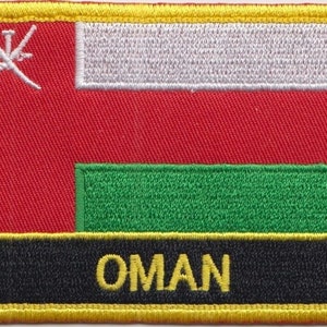 Op de afbeelding: Een geborduurde patch met de vlag van Oman. De vlag is rood met een witte horizontale streep en een groene horizontale streep aan de onderkant. De vlag heeft een wit symbool van twee gekruiste zwaarden in de linkerbovenhoek. Het woord "OMAN" staat in gele letters op een zwarte achtergrond onder de vlag.
