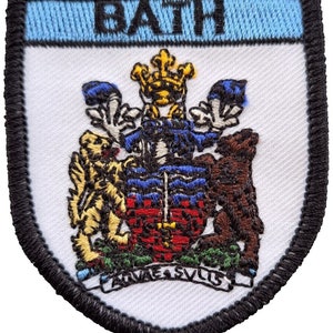 Peut inclure: Un écusson brodé blanc avec une bordure noire. L'écusson représente un blason avec une couronne, deux lions et le texte "BATH" en haut.