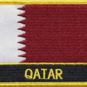Könnte beinhalten: Ein gelber gestickter Aufnäher mit einer weißen und kastanienbraunen Flagge und dem Wort "QATAR" in gelben Buchstaben.