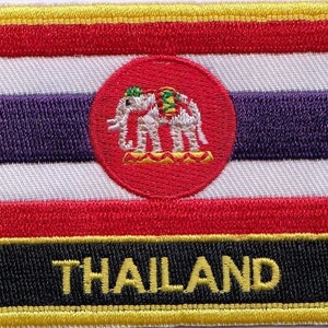 May include: An embroidered patch featuring the flag of Thailand. The patch is red, white, and blue with a white elephant in a circle in the centre. The patch has a black border with the word "THAILAND" in yellow letters.
