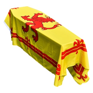 Könnte beinhalten: Ein gelber Sarg, der mit einer rot-gelben schottischen Flagge bedeckt ist. Die Flagge zeigt einen roten Löwen rampant und ein rotes Kreuz.