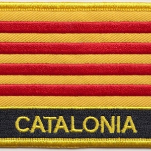May include: An embroidered patch featuring the colours of the Catalan flag, with the word "CATALONIA" in yellow lettering on a black background.