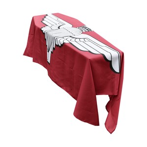 May include: A red fabric draped over a table with a white winged emblem printed on the top. The emblem is a stylized design of a pair of wings with a circle in the center.