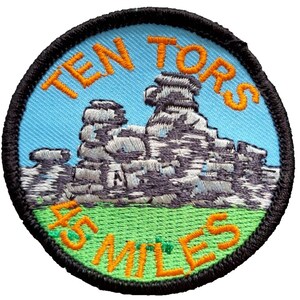 May include: A round, black-bordered patch with a blue background. The patch features an embroidered image of a rocky mountain range with the text "TEN TORS 45 MILES" in orange.