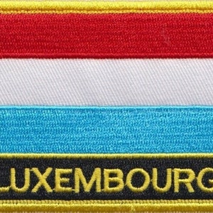 May include: An embroidered patch featuring the colours of the Luxembourg flag: red, white and light blue. The word "LUXEMBOURG" is embroidered in yellow on a black background.