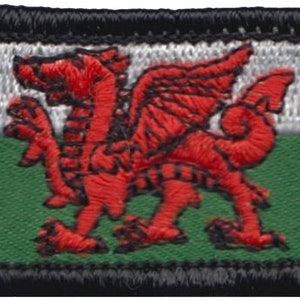 Könnte beinhalten: Gestickter Aufnäher mit der walisischen Flagge, einem roten Drachen auf weißem und grünem Hintergrund. Der Aufnäher hat einen schwarzen Rand und ist für Kleidung oder Accessoires geeignet.