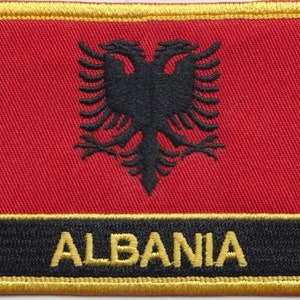 May include: A red, black, and gold embroidered patch with the Albanian flag and the word "ALBANIA" in black lettering.
