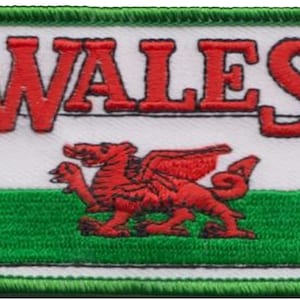 Może przedstawiać: Biała łatka z czerwonym smokiem i zielono-białymi paskami. Słowa "WALES" są wyszyte na czerwono nad flagą.