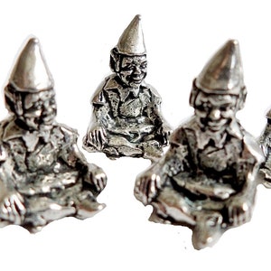 Op de afbeelding: Vijf kleine, zilverkleurige kabouterbeeldjes zijn gerangschikt op een witte achtergrond. Elke kabouter zit met gekruiste benen, draagt een puntmuts en glimlacht. De kabouters hebben gedetailleerde gezichtskenmerken en kleding.