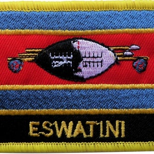 May include: A yellow embroidered patch featuring the flag of Eswatini. The flag has a red, blue and yellow horizontal stripe pattern with a black and white shield and spears in the centre. The word "ESWATINI" is embroidered in yellow on a black background at the bottom of the patch.