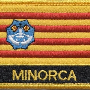 May include: A yellow and red striped fabric patch with a blue emblem featuring a white anchor and the word "MINORCA" in yellow letters.