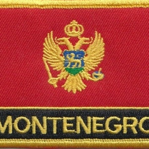May include: A red embroidered patch featuring a gold eagle and shield design. The text "MONTENEGRO" is embroidered in gold on a black background.