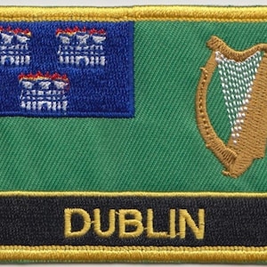 Könnte beinhalten: Ein gestickter Aufnäher in Grün und Blau mit einer goldenen Harfe und dem Wort "DUBLIN" in goldenen Buchstaben. Der Aufnäher hat einen goldenen Rand.