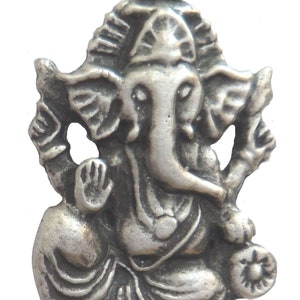 May include: A silver-colored metal pendant featuring a detailed depiction of the Hindu deity Ganesha. The pendant shows Ganesha sitting with his trunk raised and his hands in a gesture of blessing.